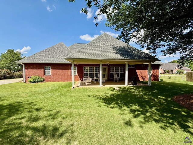back of house with a lawn, a shingled roof, a patio, and brick siding