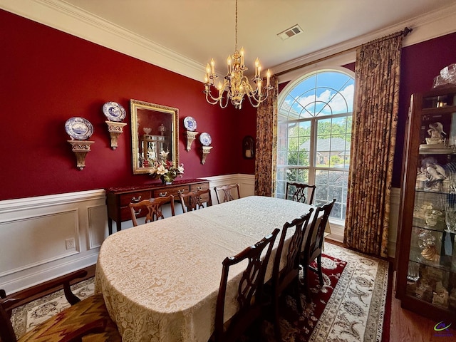 dining area with a chandelier, ornamental molding, wood finished floors, and a wainscoted wall