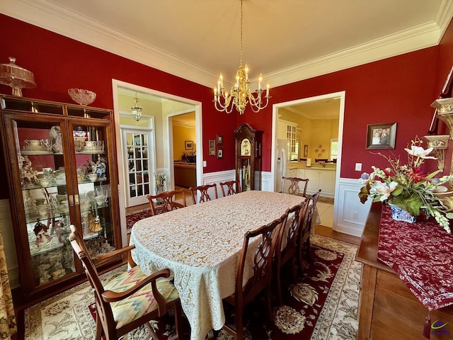 dining area with ornamental molding, a wainscoted wall, and a chandelier
