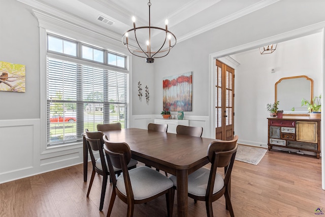dining space featuring crown molding, a chandelier, light wood-type flooring, plenty of natural light, and a wainscoted wall