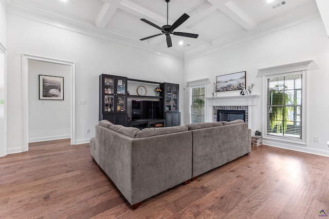 living room featuring plenty of natural light, a high ceiling, coffered ceiling, a glass covered fireplace, and a ceiling fan