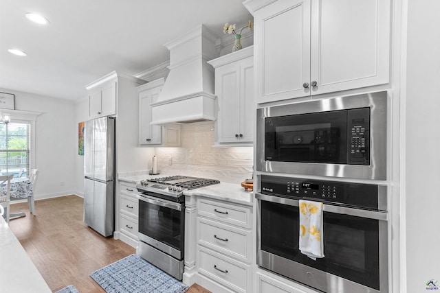 kitchen with appliances with stainless steel finishes, light wood-style floors, white cabinetry, decorative backsplash, and custom range hood