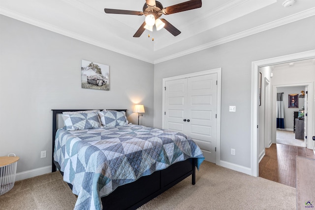 carpeted bedroom with crown molding, a tray ceiling, a closet, baseboards, and a ceiling fan