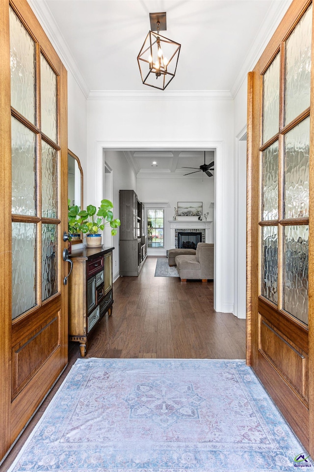 entryway with dark wood finished floors, crown molding, a glass covered fireplace, a chandelier, and a ceiling fan