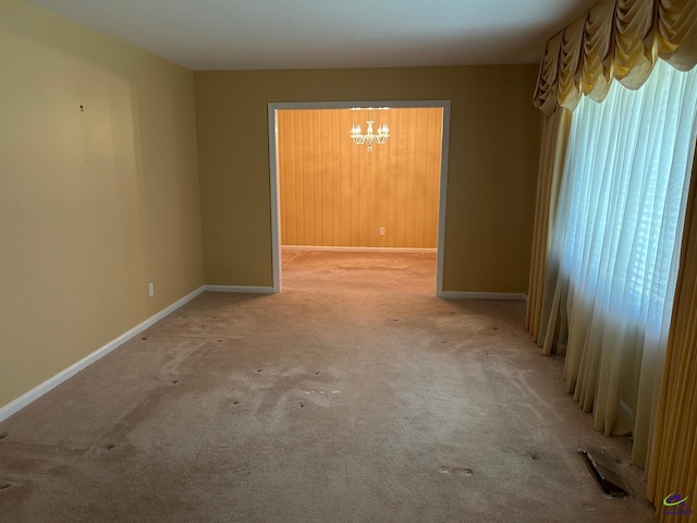 empty room with carpet flooring, a chandelier, and baseboards