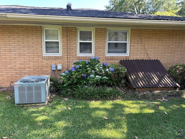 view of side of property with cooling unit, brick siding, and a yard
