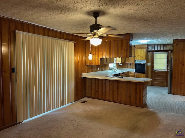 kitchen with oven, brown cabinets, light colored carpet, a peninsula, and a textured ceiling