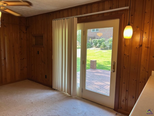 doorway with wooden walls, light colored carpet, ceiling fan, and a textured ceiling