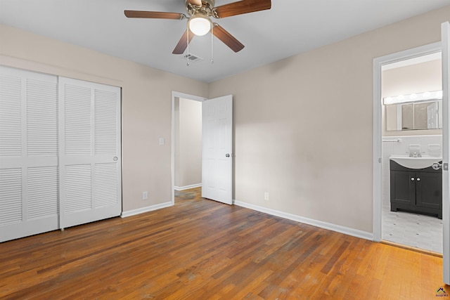 unfurnished bedroom with wood finished floors, baseboards, a closet, connected bathroom, and ceiling fan