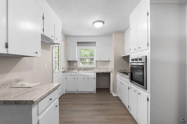kitchen with appliances with stainless steel finishes, wood finished floors, a sink, and white cabinetry