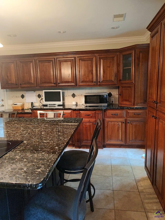 213 Falcon Crst, Warner Robins, GA 31088 - kitchen with stainless steel microwave, dark stone counters, a breakfast bar area, ornamental molding, and light tile patterned flooring