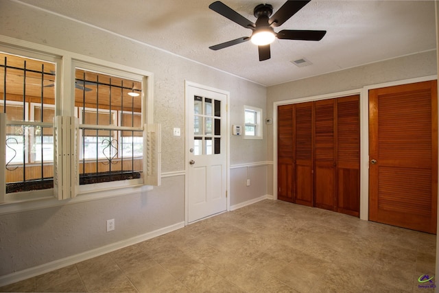 unfurnished bedroom featuring two closets, a textured ceiling, baseboards, tile patterned floors, and a ceiling fan