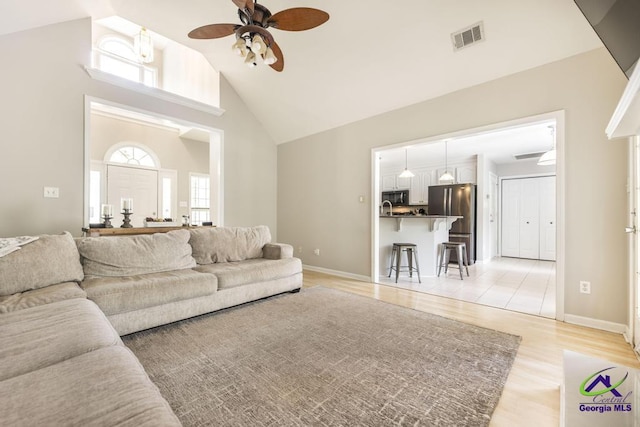 living area with high vaulted ceiling, a ceiling fan, light wood-type flooring, and baseboards