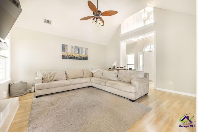 living area featuring a ceiling fan, high vaulted ceiling, light wood-style flooring, and baseboards