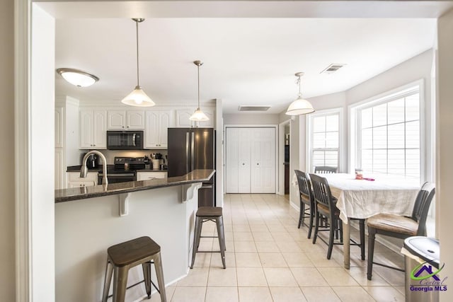 kitchen featuring appliances with stainless steel finishes, a kitchen bar, dark stone countertops, light tile patterned floors, and pendant lighting