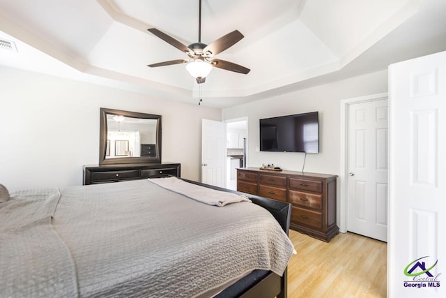 bedroom featuring a tray ceiling, light wood finished floors, and ceiling fan