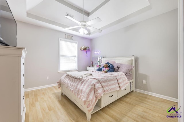 bedroom with a tray ceiling, light wood-type flooring, and baseboards
