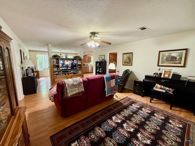 living room with light wood-style flooring, a ceiling fan, and a textured ceiling
