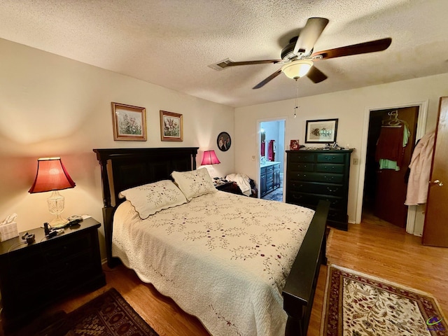 bedroom featuring wood finished floors, a textured ceiling, ceiling fan, and ensuite bath