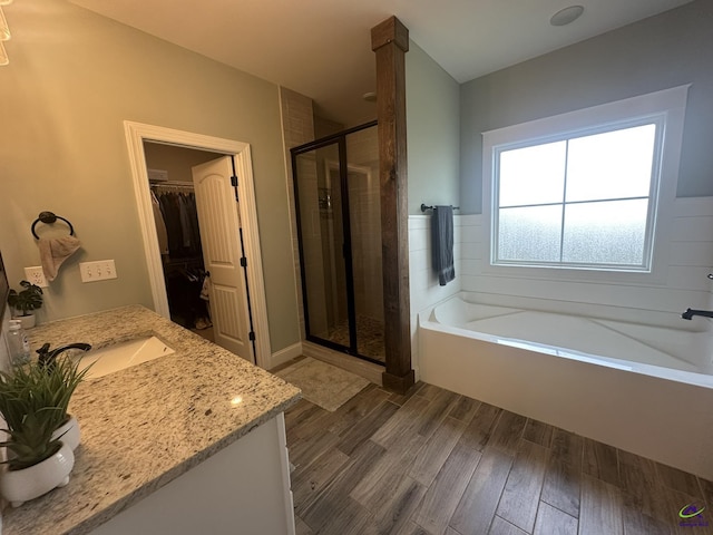 bathroom with a stall shower, a walk in closet, a bath, wood finished floors, and vanity