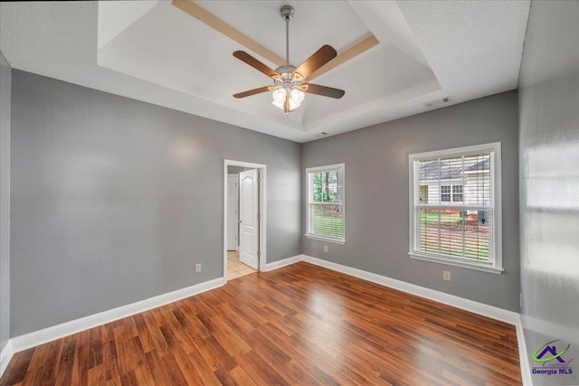unfurnished room with a tray ceiling, wood finished floors, a ceiling fan, and baseboards