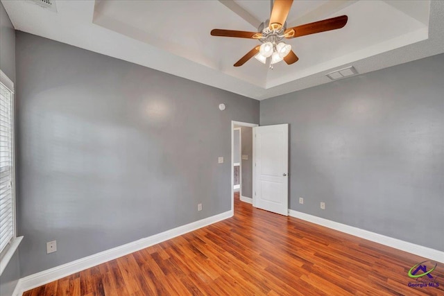 spare room featuring a tray ceiling, wood finished floors, baseboards, and a ceiling fan