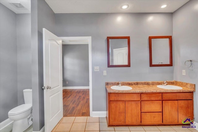 bathroom featuring toilet, tile patterned flooring, double vanity, baseboards, and recessed lighting
