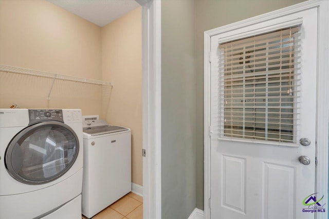 washroom with washing machine and clothes dryer, light tile patterned floors, and baseboards