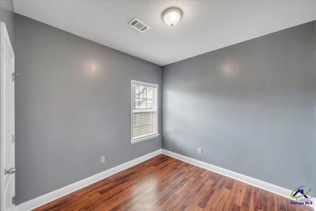empty room featuring dark wood-type flooring, baseboards, and a textured ceiling