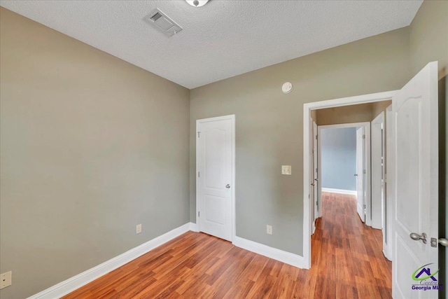 unfurnished bedroom featuring wood finished floors, baseboards, and a textured ceiling