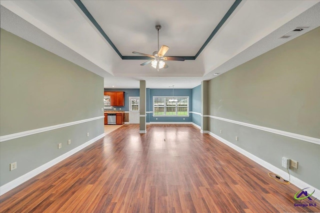 unfurnished living room featuring a raised ceiling, a ceiling fan, a chandelier, and baseboards