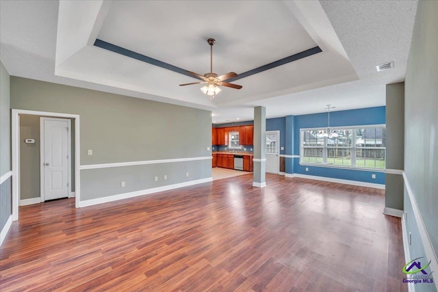 unfurnished living room with a tray ceiling, baseboards, ceiling fan, and a chandelier