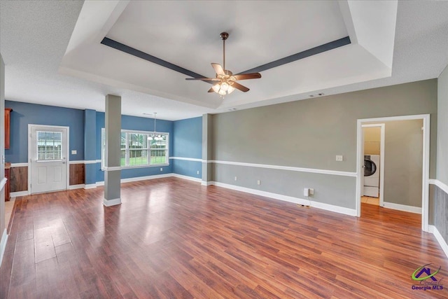 empty room featuring a raised ceiling, washer / clothes dryer, a ceiling fan, and wood finished floors