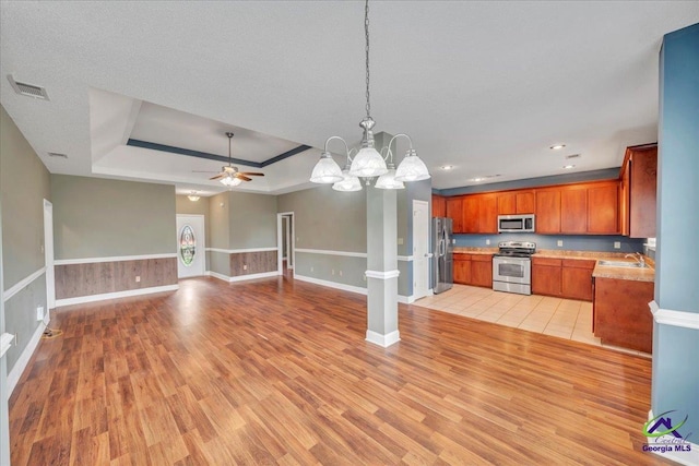 kitchen featuring stainless steel appliances, a raised ceiling, light wood-type flooring, open floor plan, and light countertops
