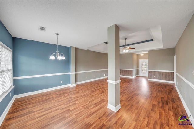 spare room with a tray ceiling, wood finished floors, ceiling fan, a chandelier, and baseboards
