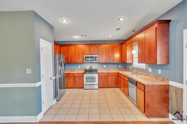 kitchen featuring appliances with stainless steel finishes, a sink, light countertops, brown cabinetry, and recessed lighting
