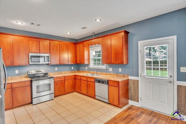 kitchen with stainless steel appliances, a sink, light countertops, brown cabinetry, and recessed lighting