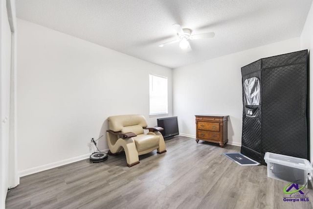 living area with ceiling fan, wood finished floors, a textured ceiling, and baseboards