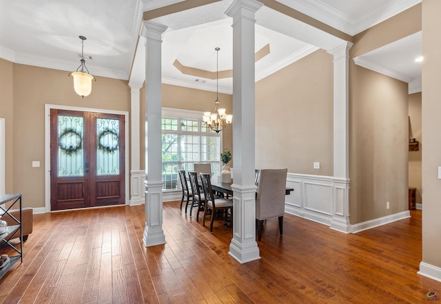 foyer with hardwood / wood-style floors, ornate columns, ornamental molding, wainscoting, and a decorative wall