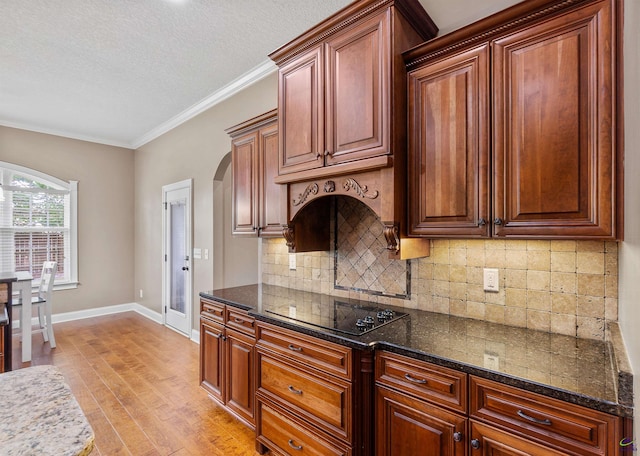 kitchen with black electric cooktop, light wood finished floors, backsplash, a textured ceiling, and arched walkways