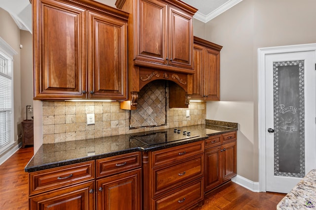 kitchen with black electric cooktop, ornamental molding, dark wood-style floors, tasteful backsplash, and dark stone counters
