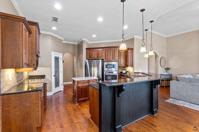 kitchen with stainless steel appliances, arched walkways, a sink, a kitchen island, and brown cabinets