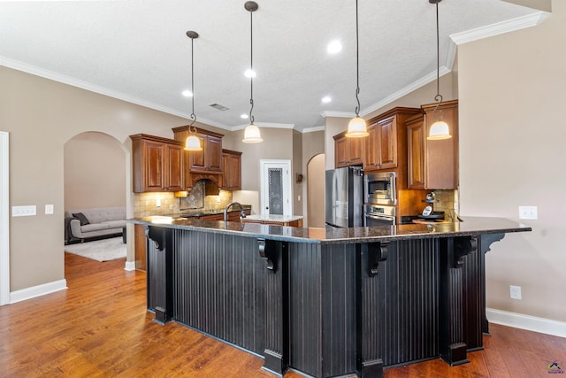 kitchen featuring arched walkways, stainless steel appliances, brown cabinetry, backsplash, and a textured ceiling