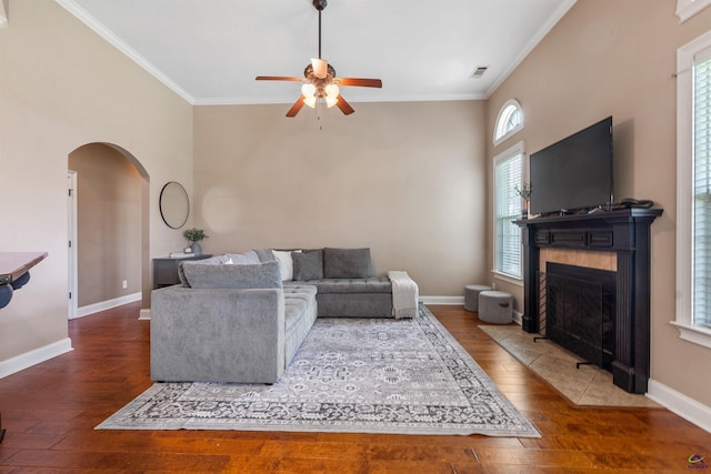 living area with a ceiling fan, arched walkways, wood-type flooring, crown molding, and baseboards