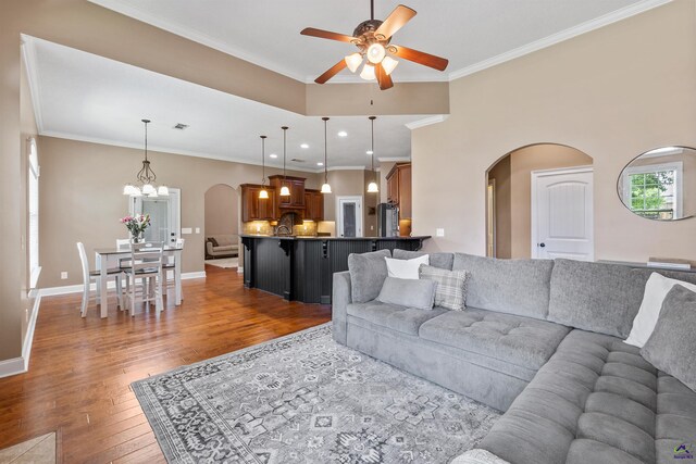living room featuring arched walkways, a ceiling fan, light wood-style floors, a chandelier, and ornamental molding