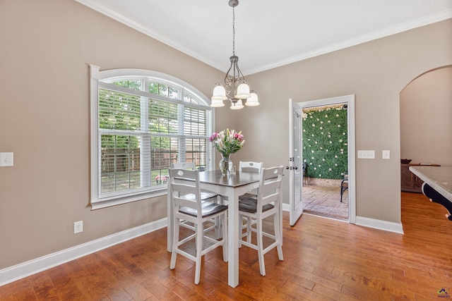 dining room featuring arched walkways, ornamental molding, baseboards, wood-type flooring, and a chandelier