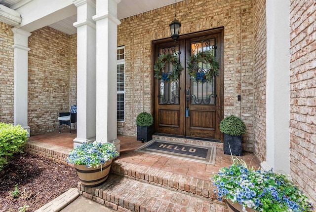 view of exterior entry featuring covered porch, brick siding, and french doors