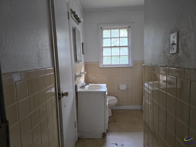 half bath with tile walls, toilet, wainscoting, vanity, and ornamental molding