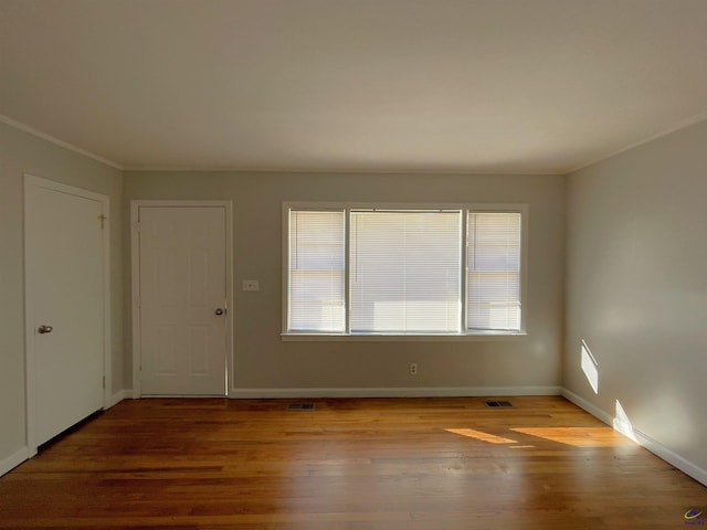 empty room featuring plenty of natural light, crown molding, wood finished floors, and baseboards