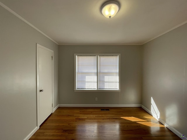 spare room featuring wood finished floors, crown molding, and baseboards